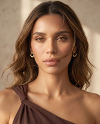 Gold circle stud earrings featuring a sculptural open-circle silhouette and polished finish on a model