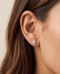 Close-up of a woman wearing a small gold stud earring with a teardrop-shaped cubic zirconia stone.