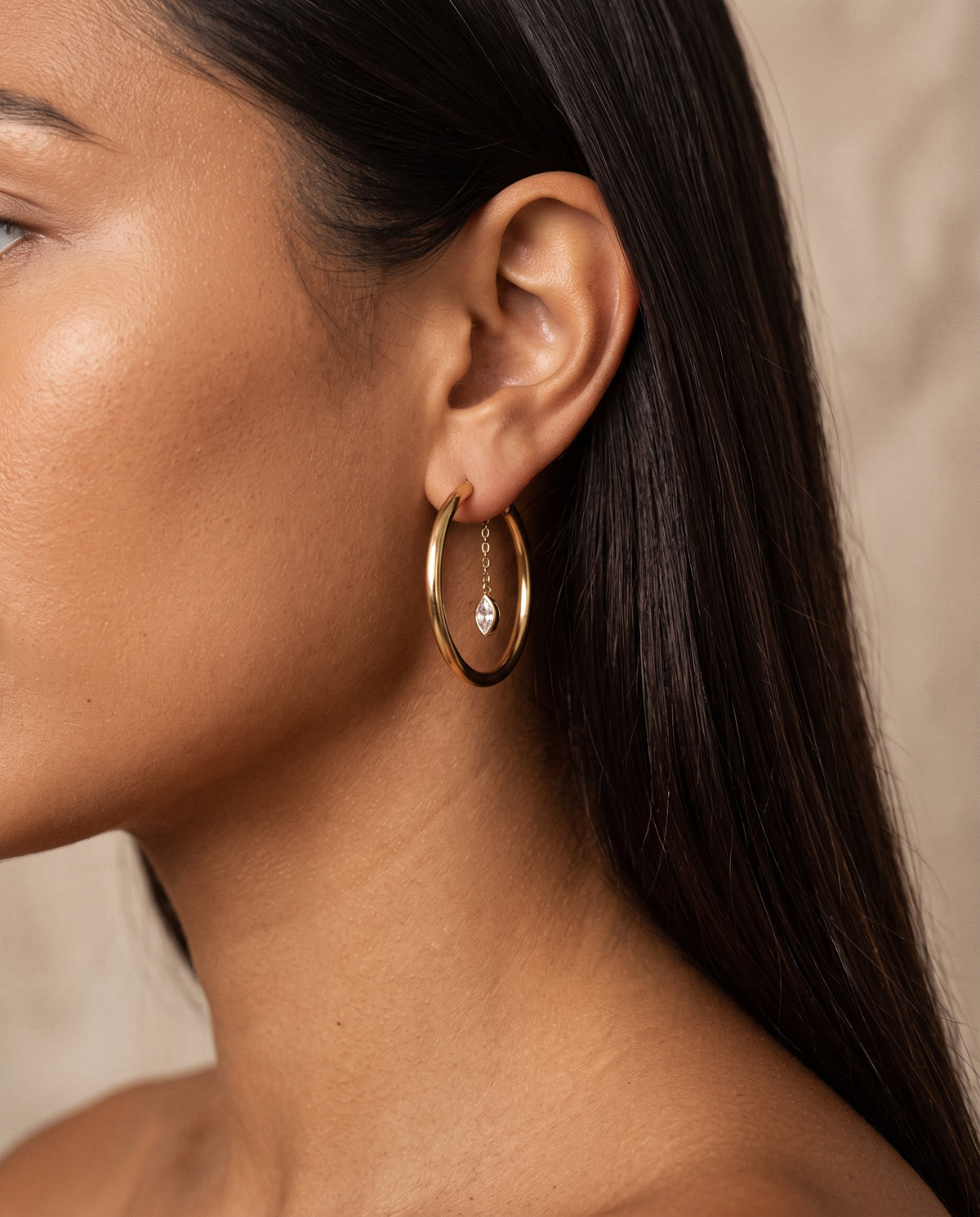 Woman wearing gold hoops with marquise CZ charms suspended from delicate chains.