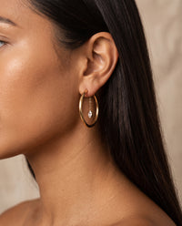 Woman wearing gold hoops with marquise CZ charms suspended from delicate chains.