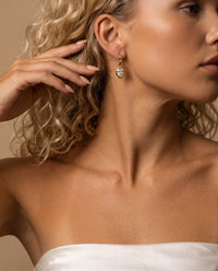 Woman wearing sculptural gold teardrop earrings with pear-cut cubic zirconia stones and molten frames.