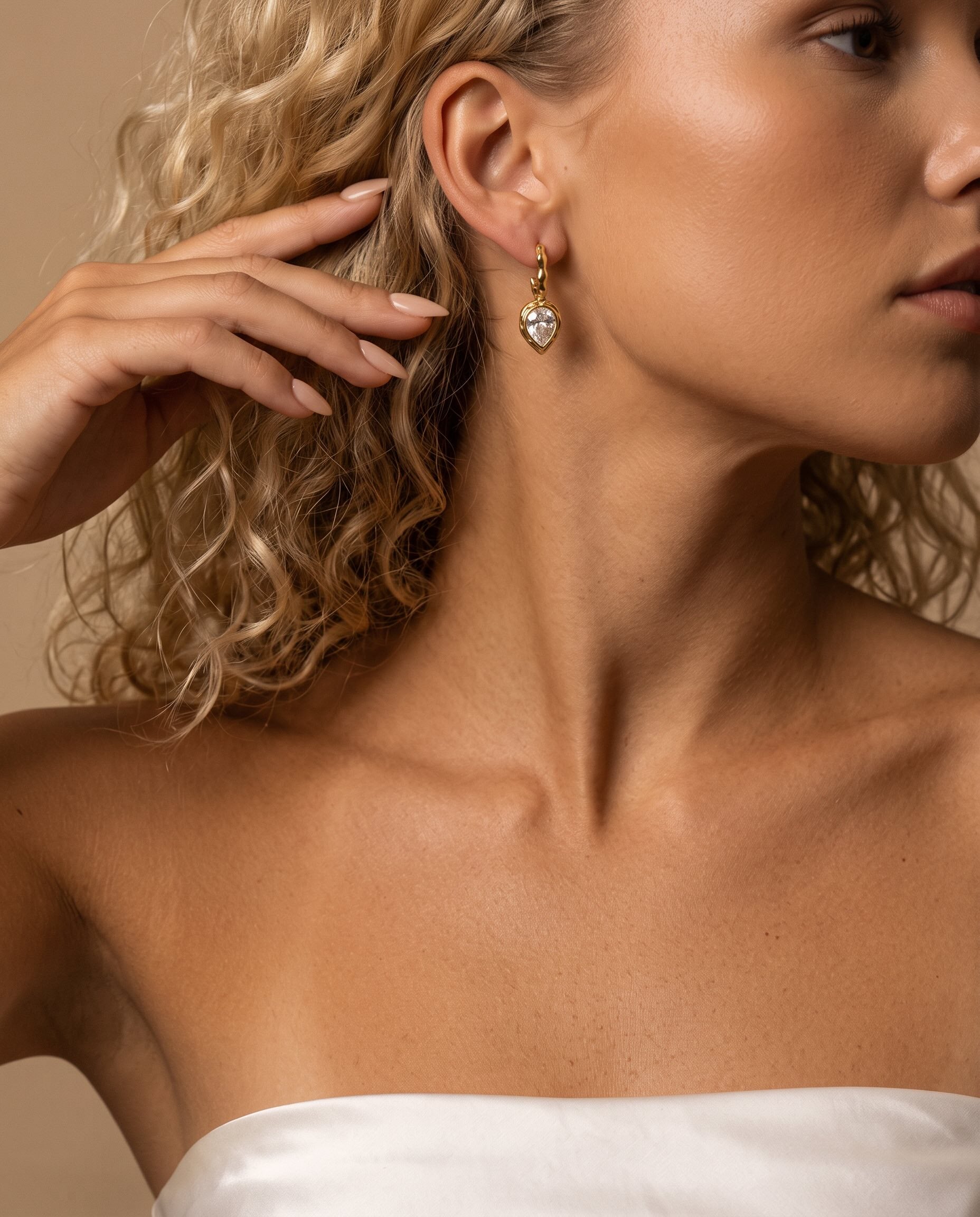 Woman wearing sculptural gold teardrop earrings with pear-cut cubic zirconia stones and molten frames.