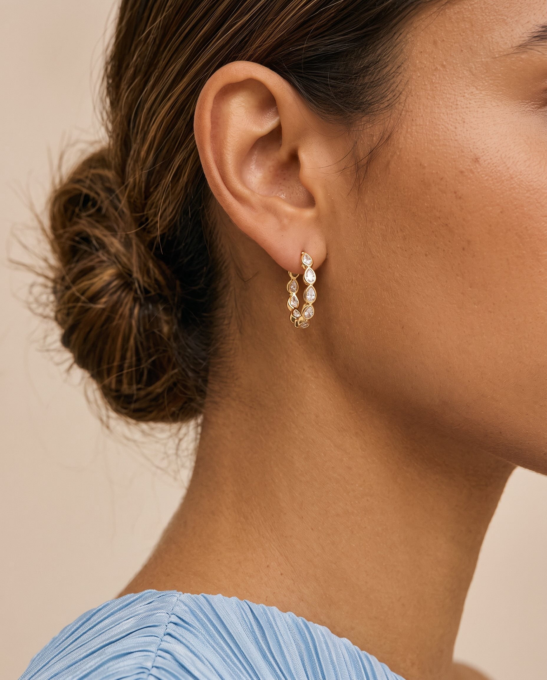 Close up of woman wearing gold tennis hoops with pear-shaped cubic zirconia stones.