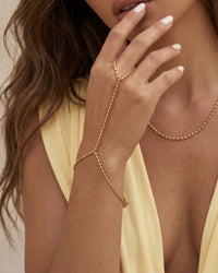 Gold beaded hand chain featuring an elongated bead chain design connecting the finger and wrist.